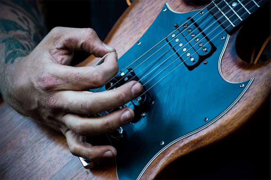 Image of a man playing an electric guitar using a guitar pick. Source: pixabay