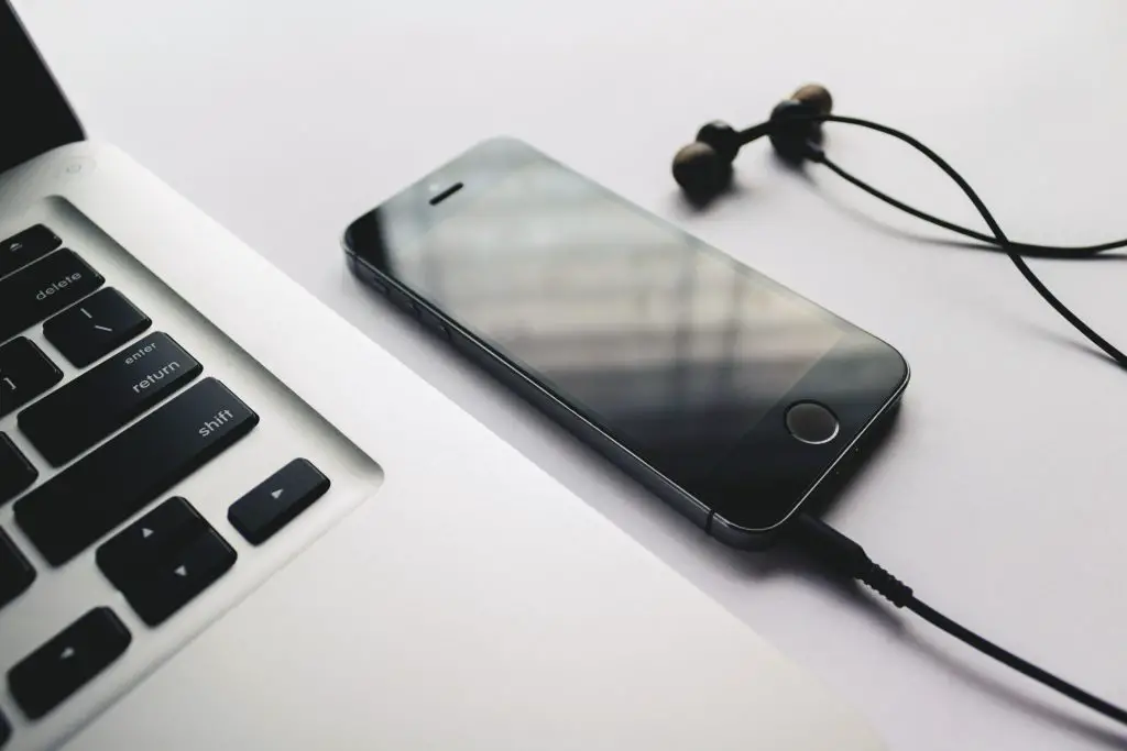 Image of laptop, and an iphone connected with a black earphones. Source: rupixen com, unsplash