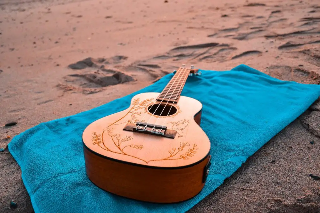 Image of a brown guitar with designs lying on a beach towel on the sand. Source: nuno campos, pexels