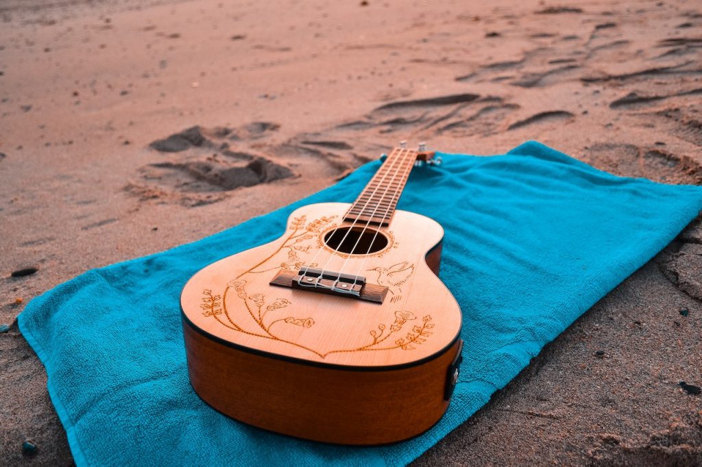 Image of a brown guitar with designs lying on a beach towel on the sand. Source: nuno campos, pexels