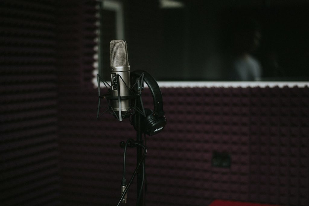 Image of a condenser microphone in a stand with a headphone beside it. Source: john wolf, pexels