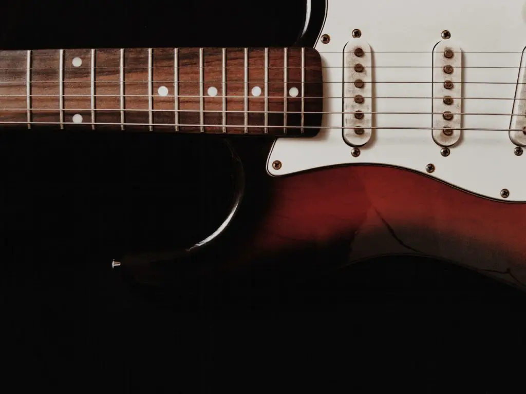 Image of a guitar in a red and white color with complete strings on it. Source: andre moura, pexels