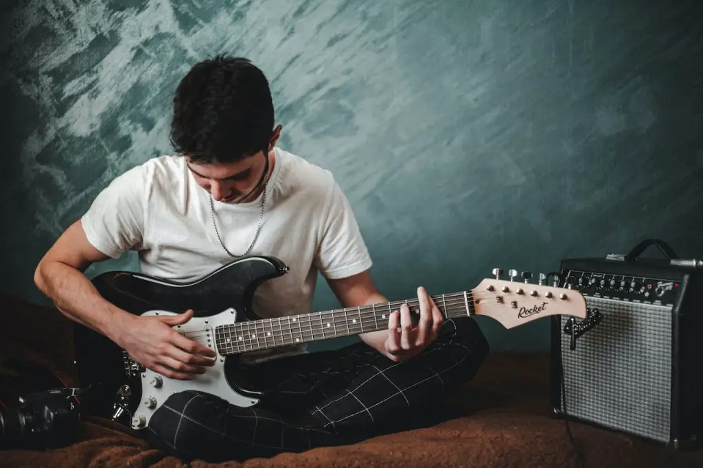Image of a man playing an electric guitar with an amplifier beside him. Source: alexandr ivanov, pexels