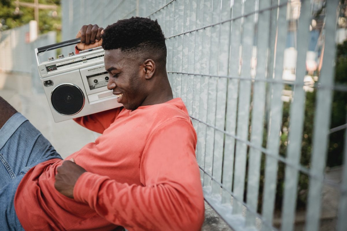 Image of a man sitting while holding a radio and listening to it. Source: Budgeron Bach, Pexels