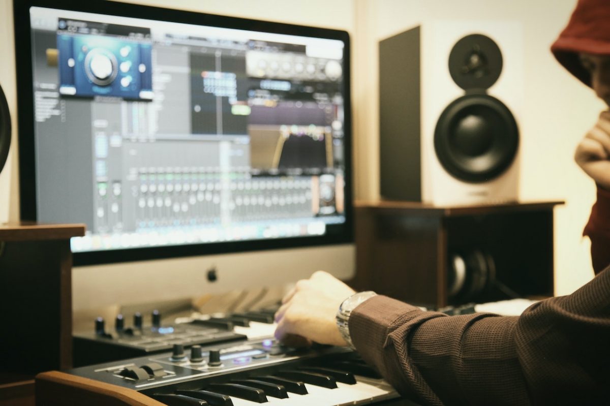 Image of a person using a midi controller a speaker and a computer. Source: Amin Asbaghipour, Pexels