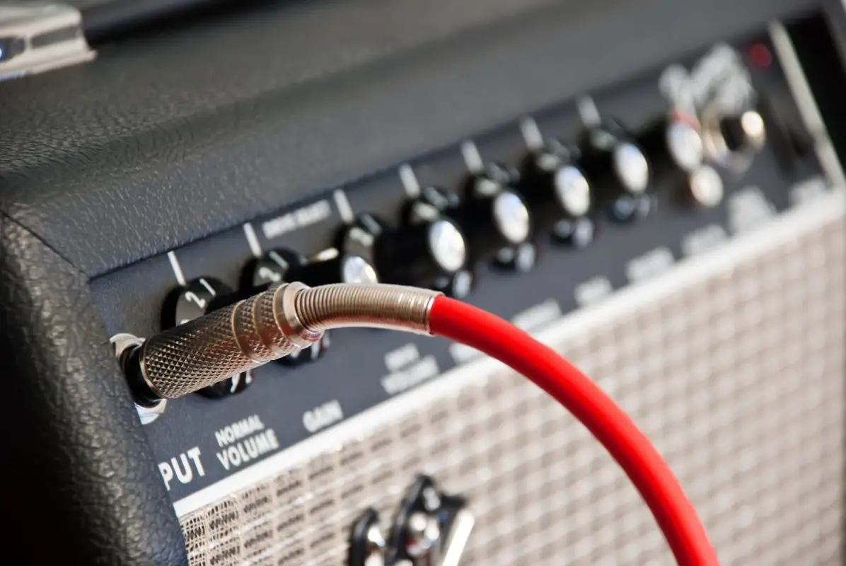 Image of red guitar cable connected to a black amplifier. Source: Adobe Stock