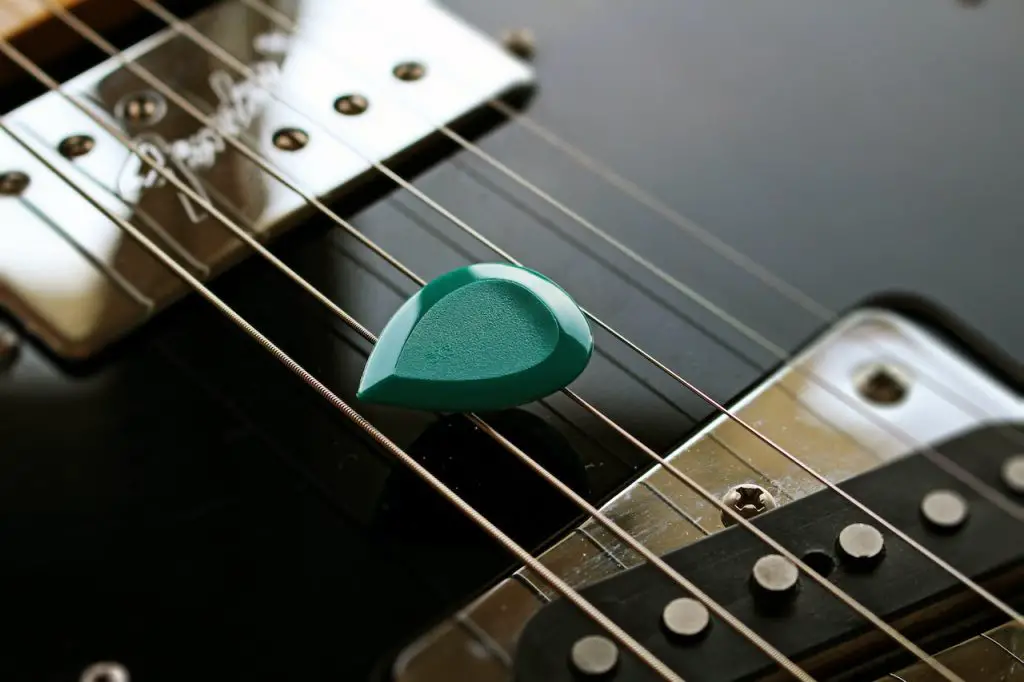 Image of a black guitar and a green guitar pick. Source: rombo, pexels