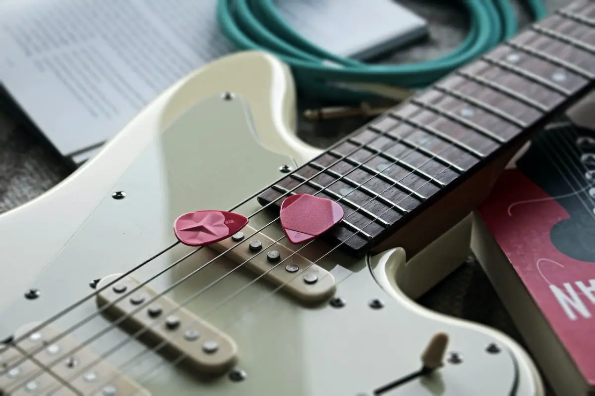 Image of a guitar and a pink guitar pick on top. Source: rombo, pexels
