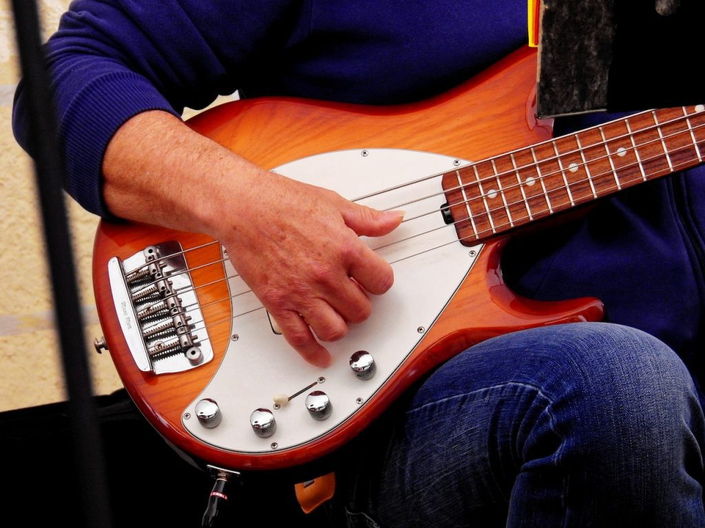 Image of a man playing a brown and white bass guitar. Source: pixabay