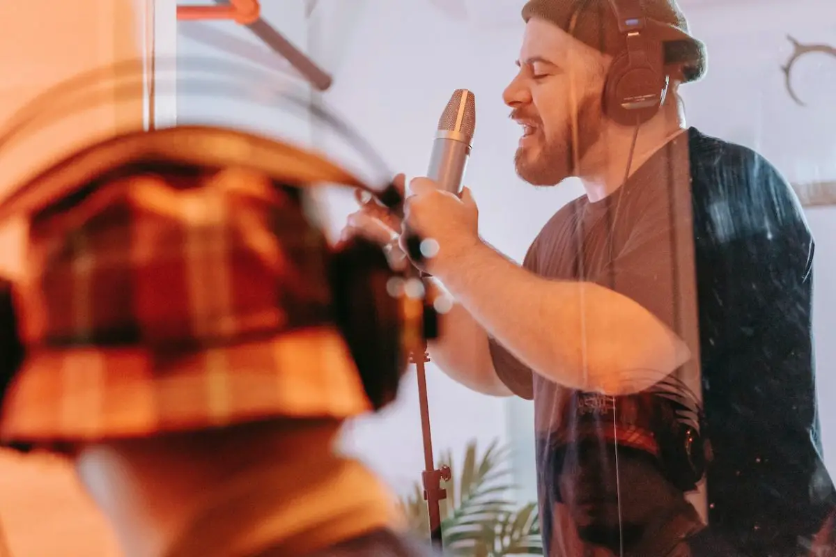 Image of a man singing while inside a vocal booth. Source: anna pou, pexels