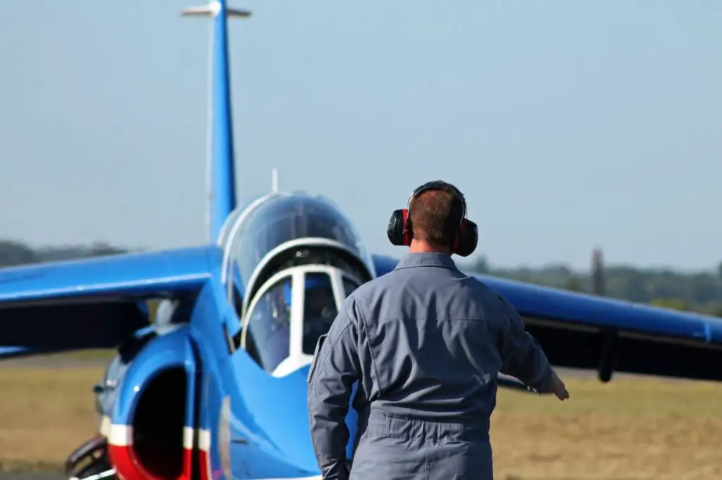 Image of a man using a noise canceling headphones in front of a blue airplane. Source: arnaud audoin, pexels