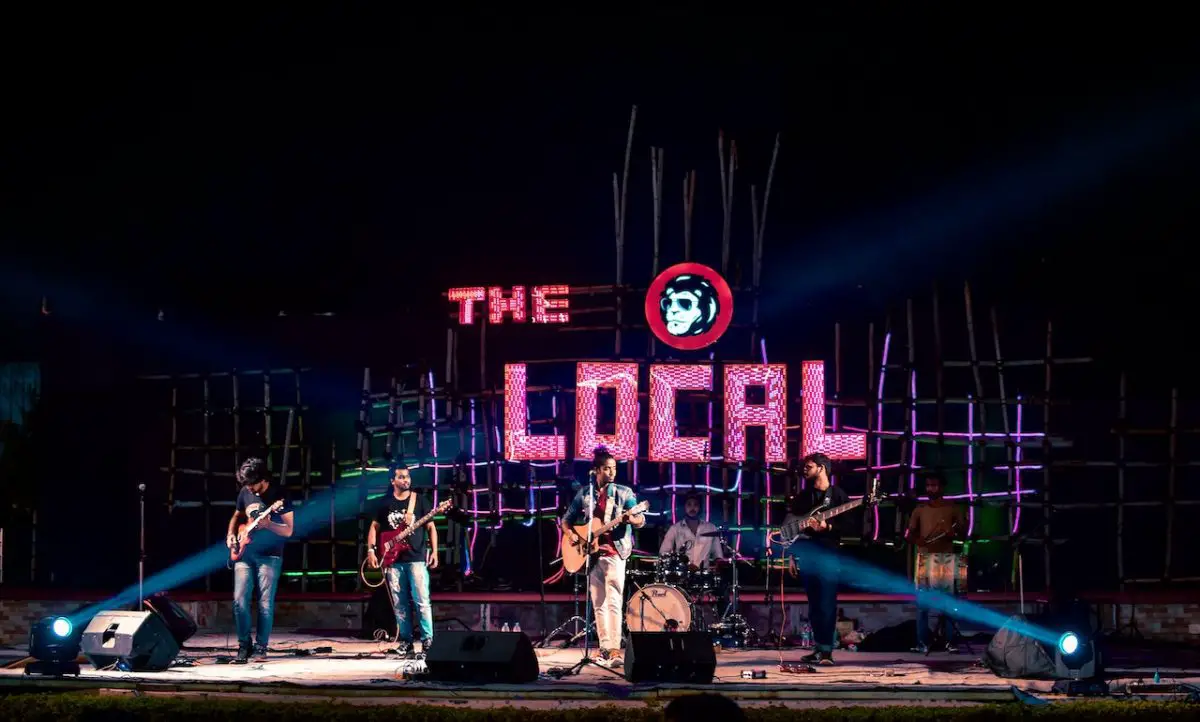 Image of a performing band with a band logo at the back. Source: vivaan gupta, pexels