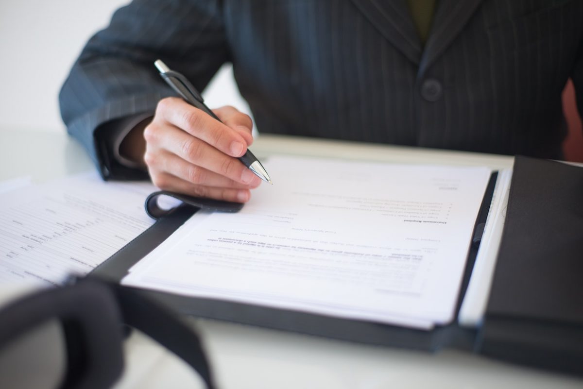 Image of someone holding a pen with documents on a folder. Source: Kampus Production, Pexels