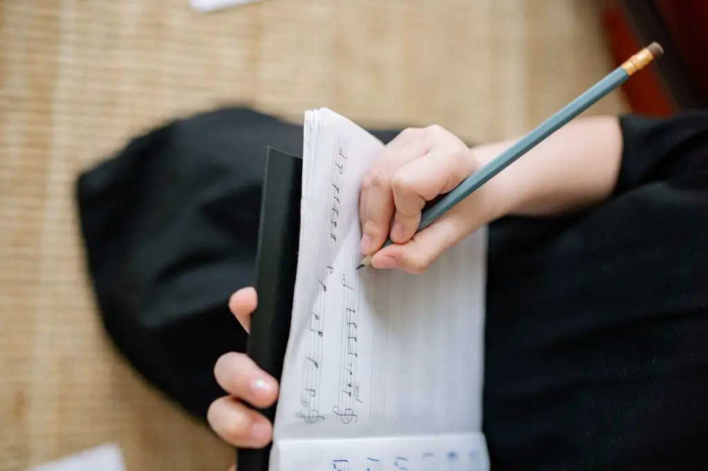 Image of someone writing on a song notebook. Source: yan krukau, pexels