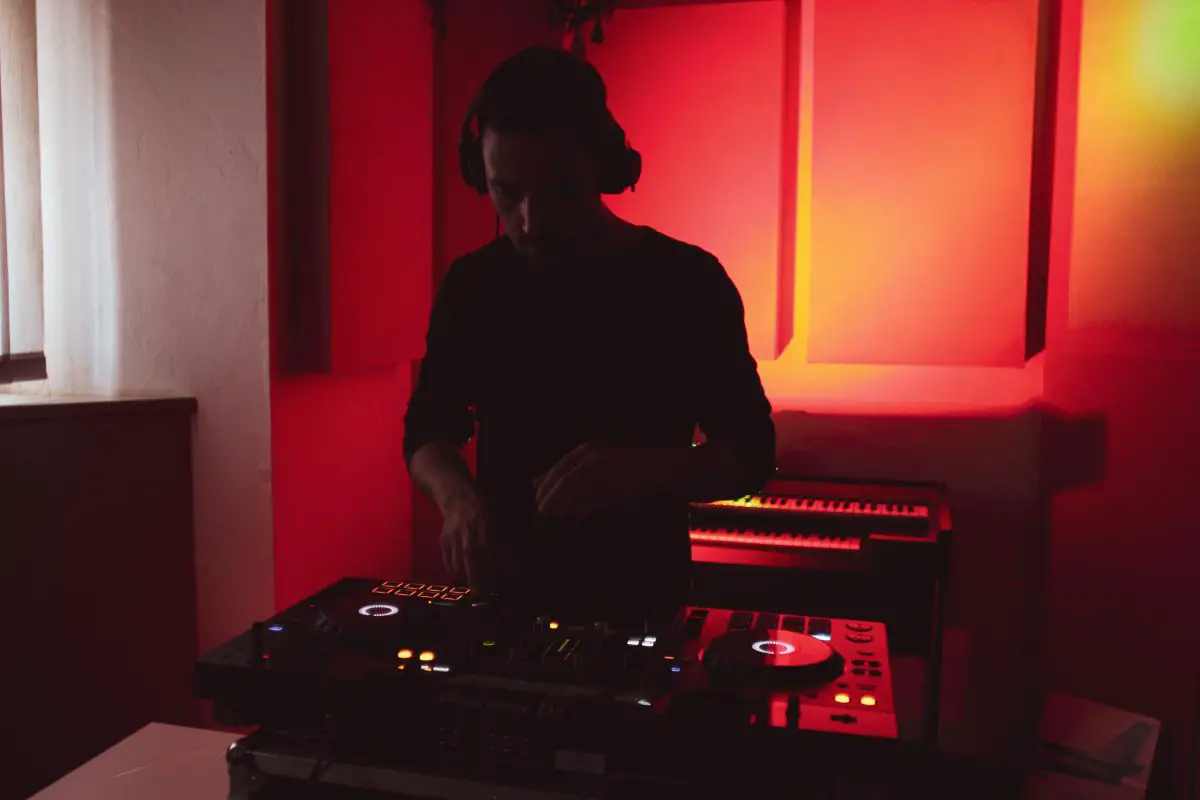 Image of a man mixing music in a room with red lights. Source: pexels