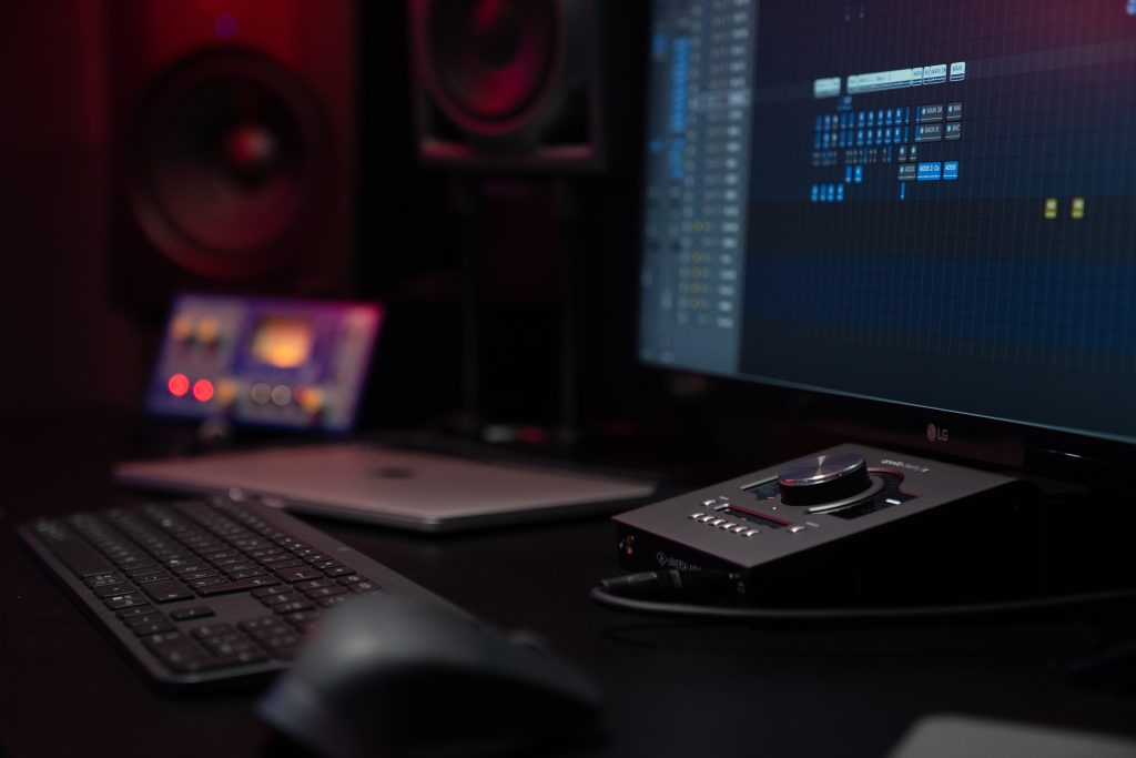 Image of a monitor a keyboard and an audio interface device on a table. Source: unsplash