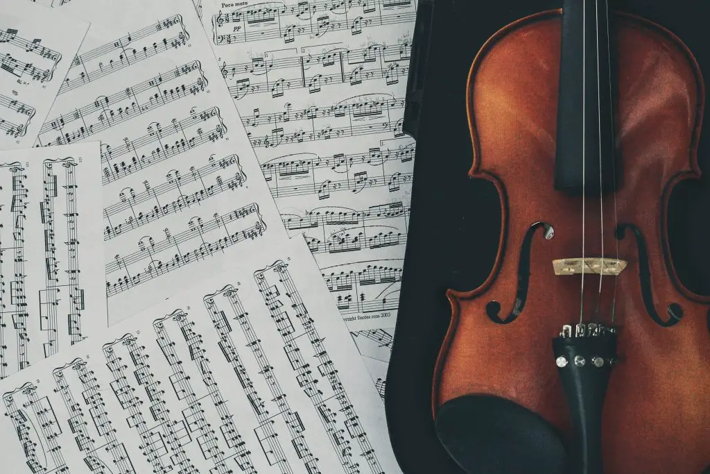 Image of a violin with broken strings on a case beside the musical notes. Source: unsplash