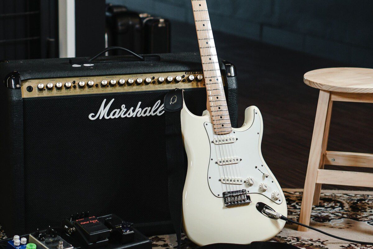 Image of a white guitar leaning on an amplifier. Source: unsplash