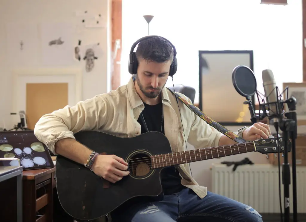 Man in a recording studio tuning his acoustic guitar. Source: pexels