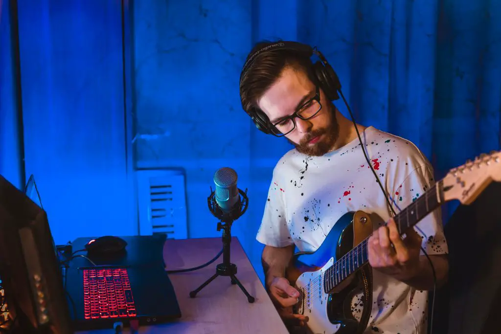 Musician wearing headphones and playing electric guitar in his home recording studio. Source: unsplash