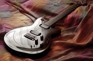 Image of a black electric guitar on a bed. Source: Pexels