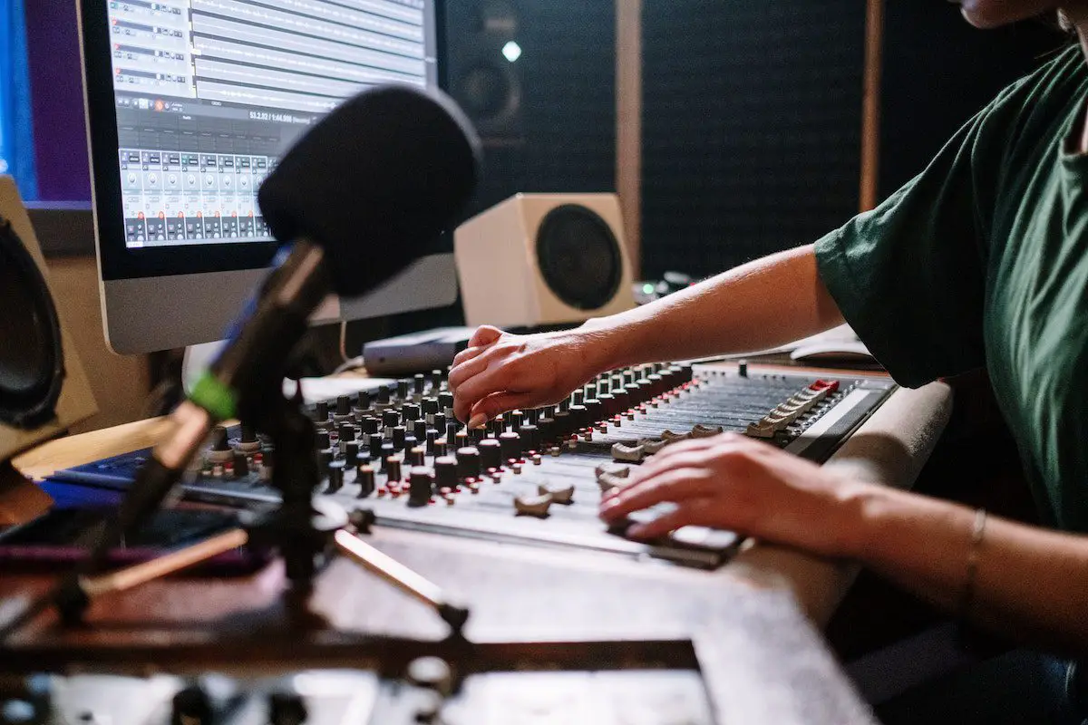 Image of a man adjusting an audio mixer in front of a computer. Source: pexels