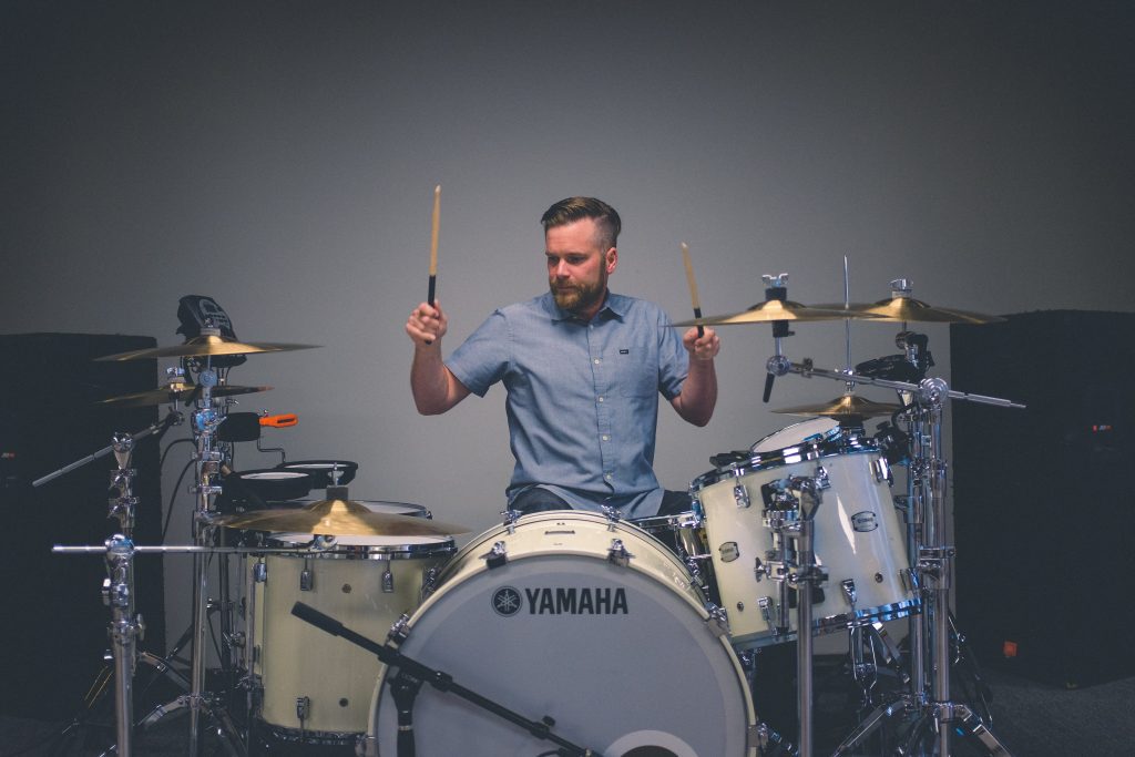 Image of a man holding his drum sticks, sitting and ready to play. Source: unsplash