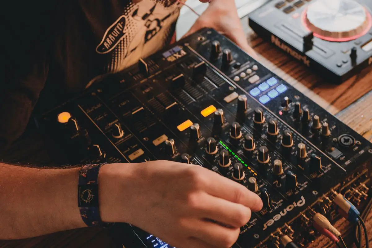 Image of a man in black playing with his pioneer audio mixer. Source: unsplash