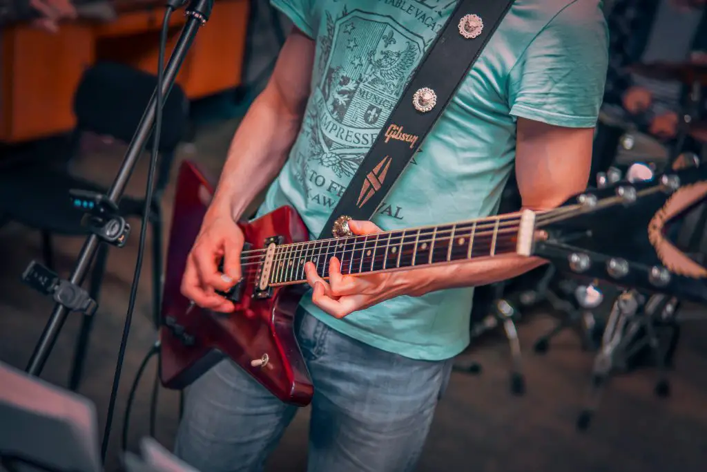 Image of a man in blue denim jeans playing a red electric guitar. Source: pexels