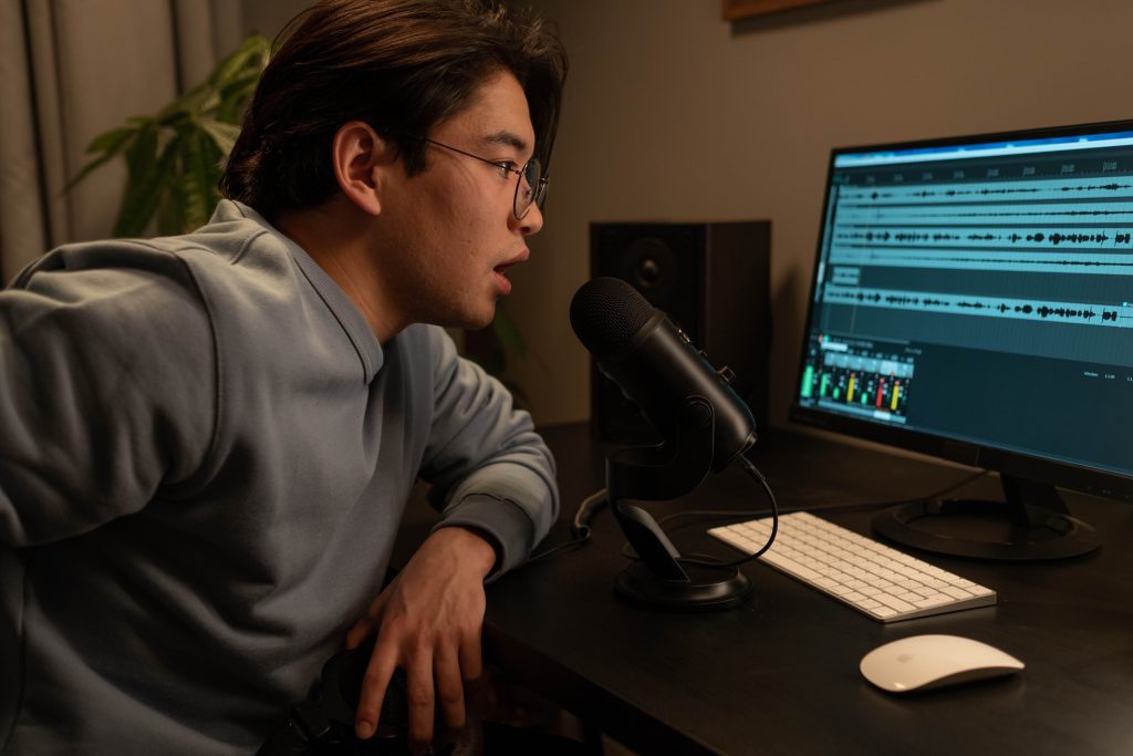 Image of a man in gray sweater sitting at the table in front of a monitor. Source: pexels