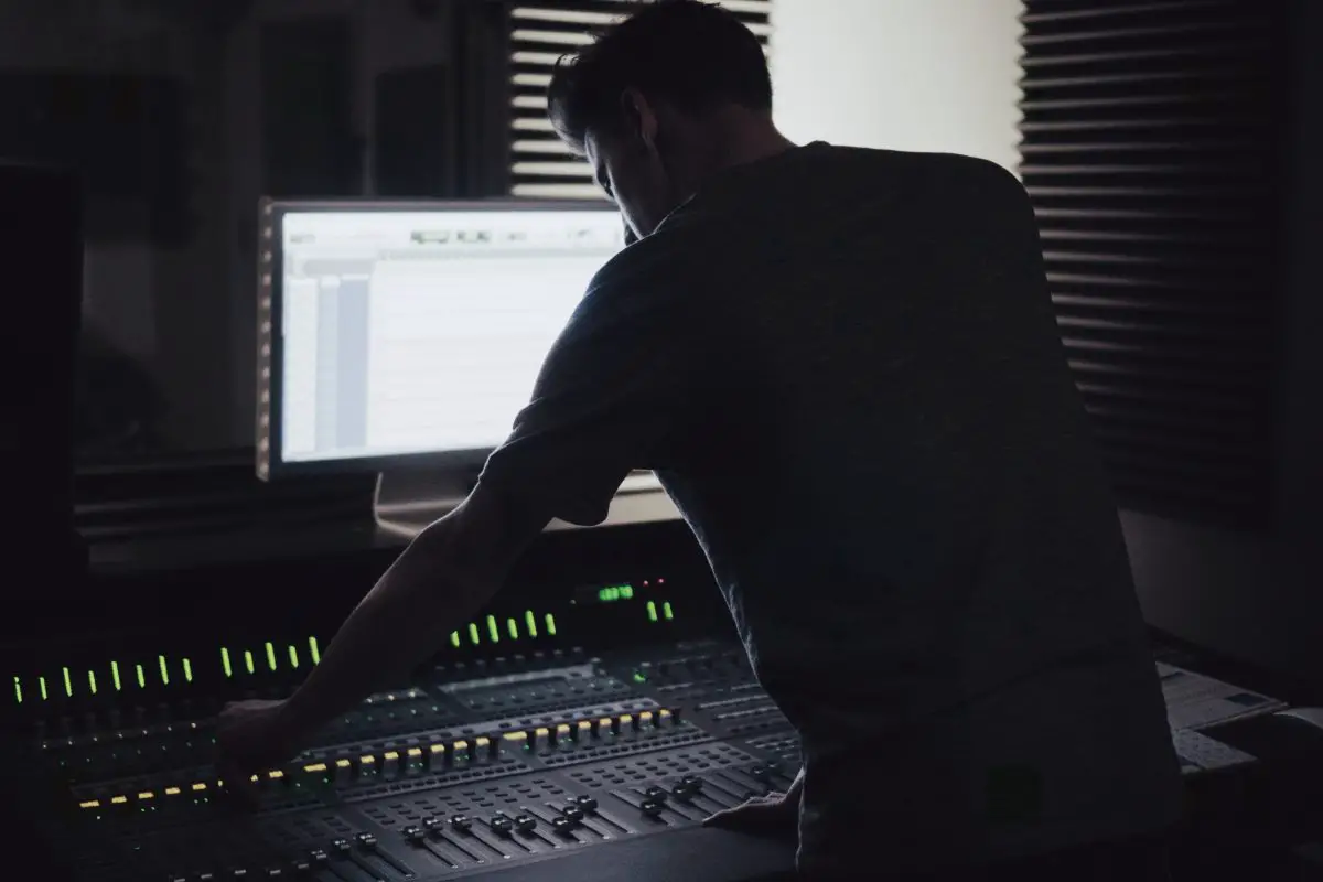 Image of a man operating an audio mixer inside a dark room. Source: unsplash