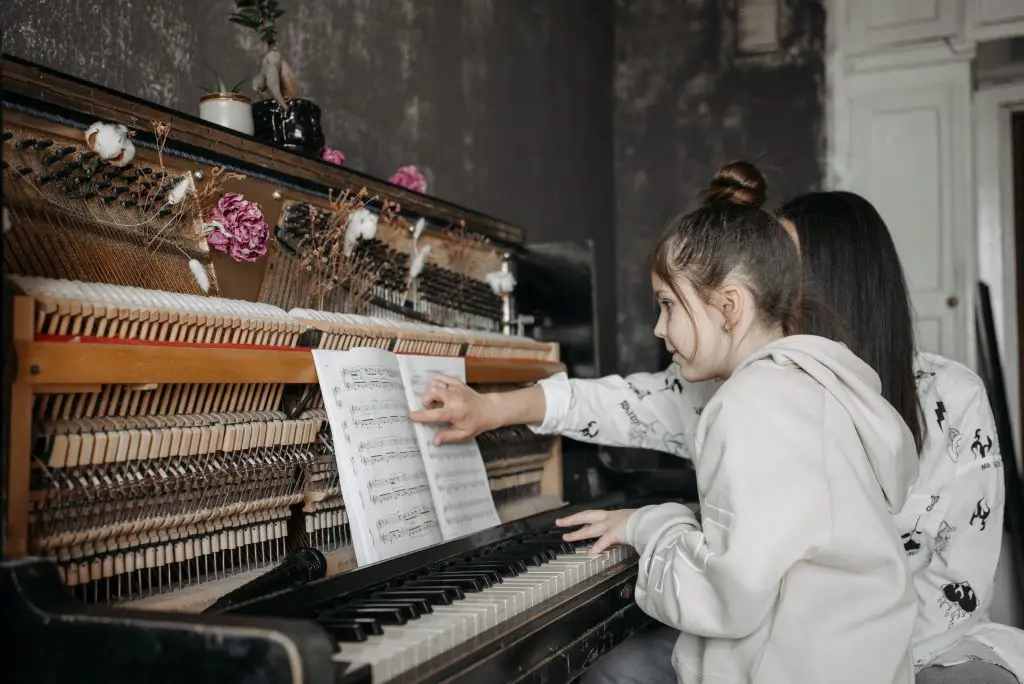Image of a woman in a white long-sleeve shirt playing the piano. Source: pexels