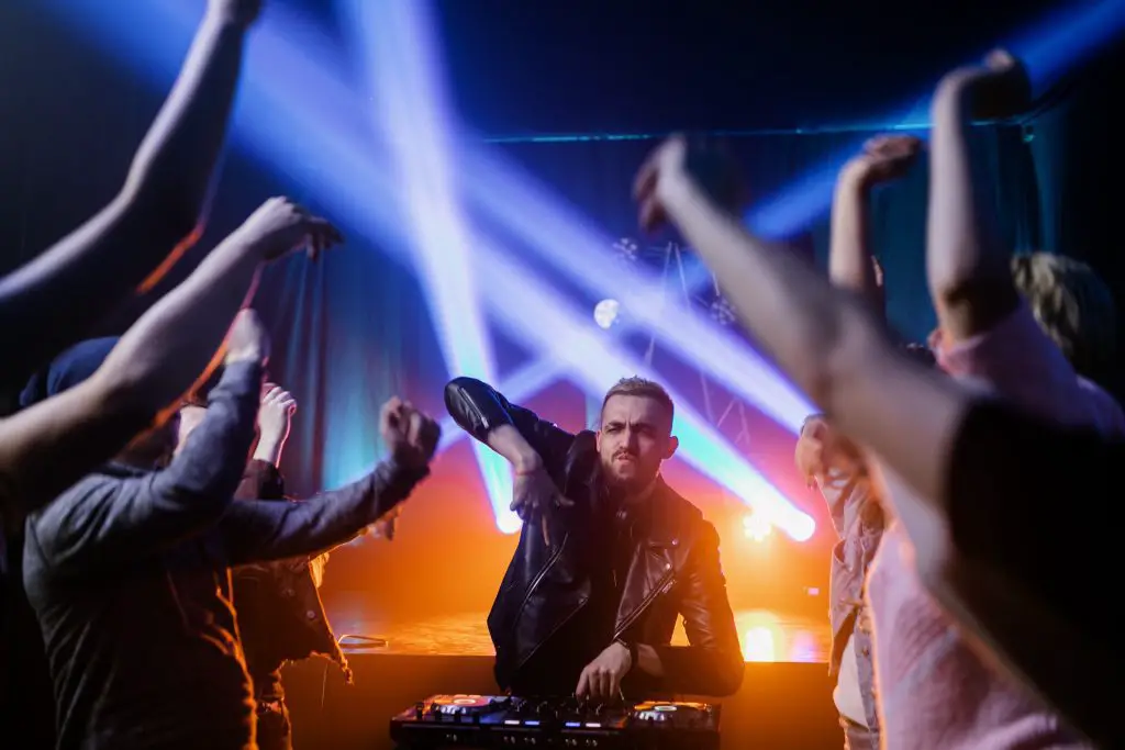 A DJ playing with people dancing. Source: Pexels