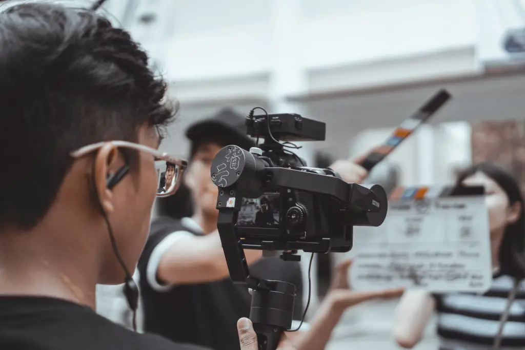 A filmmaker shooting with a camera in front of actors. Source: Unsplash