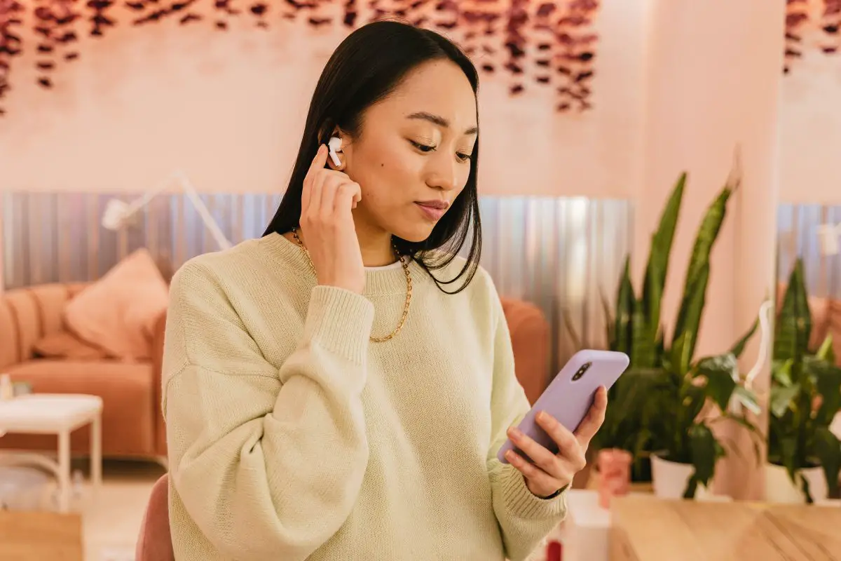 Image of woman wearing wireless earphones and holding her phone. Source: Pexels.