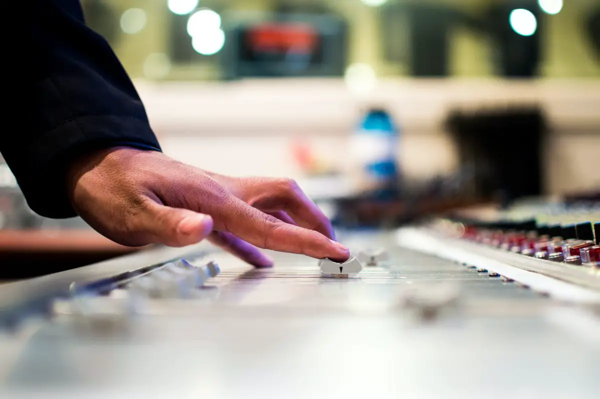 Image of a hand controlling an audio mixer.
