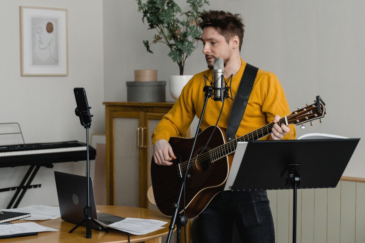 Image of a man singing and playing the guitar in front of a laptop and cellphone.