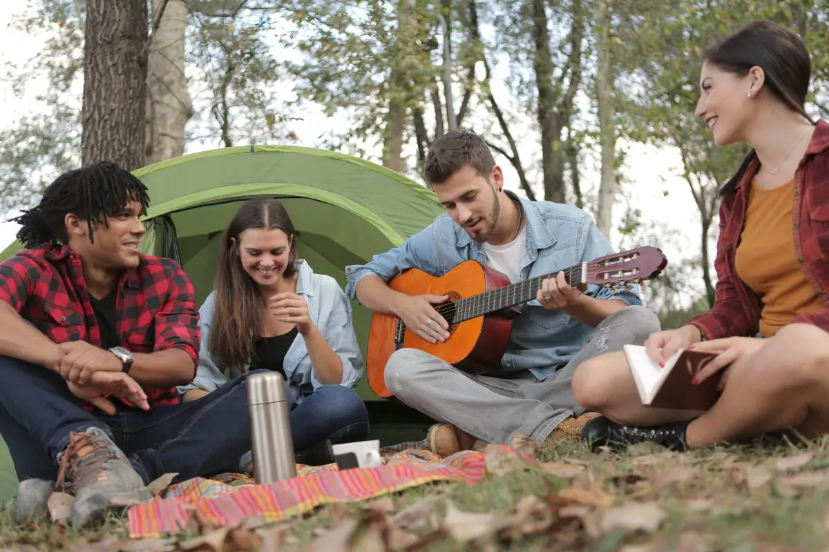 A man playing acoustic guitar with three friends sitting on the grass. Source: pexels