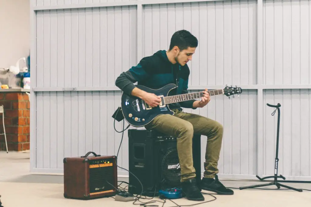 A man sitting on a speaker and playing the electric guitar. Source: unsplash