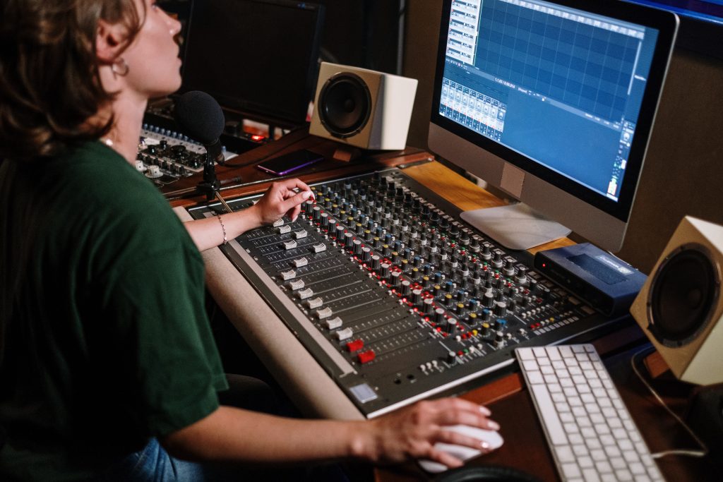 A woman working on a computer with an audio mixer. Source: pexels