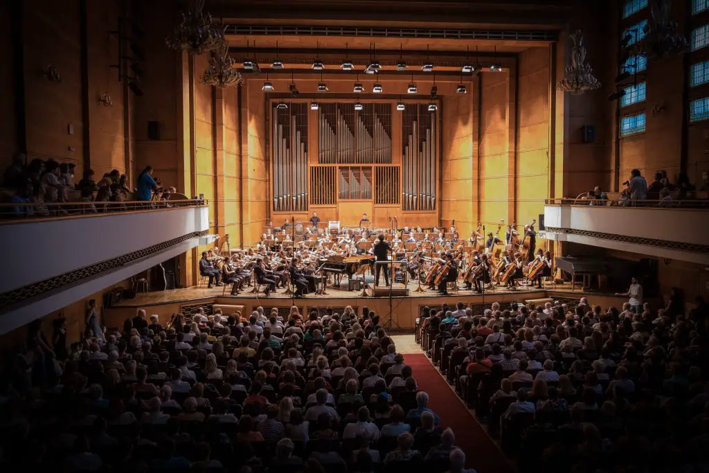 An orchestra on stage with a packed audience. Source: unsplash