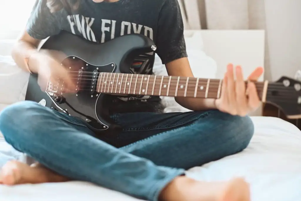 Image of a guitarist playing an electric guitar while sitting on a bed. Source: unsplash