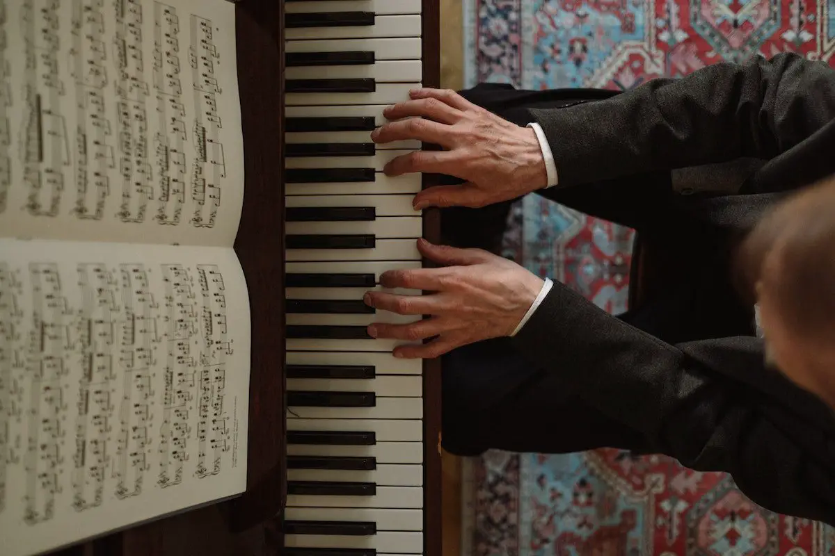 Image of a man playing the piano while reading a music sheet. Source: pexels