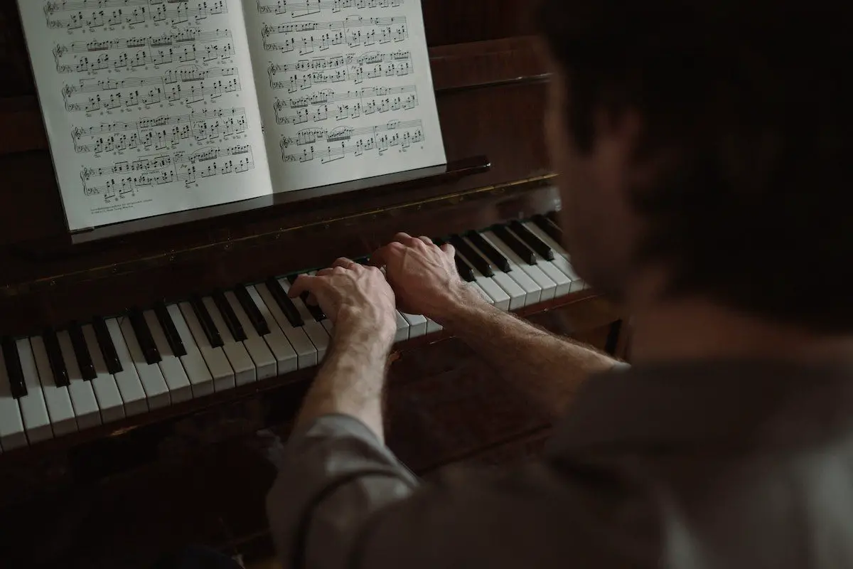 Image of a man playing the piano while reading sheet music pexels