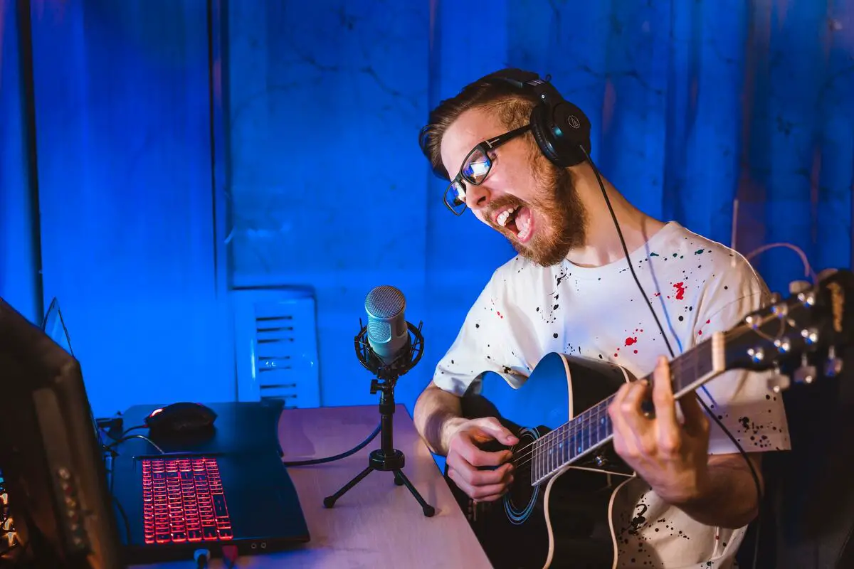 Image of a man recording with a mic while playing the guitar. Source: unsplash