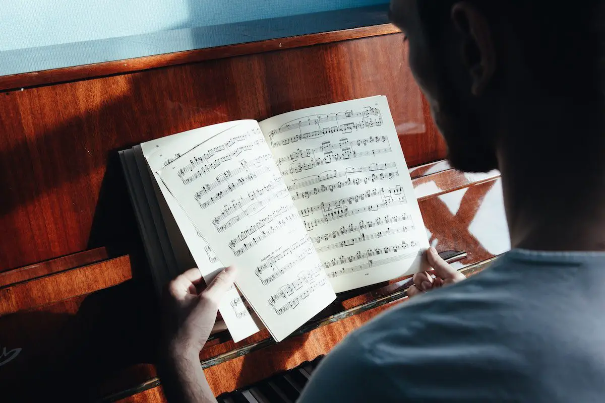 Image of a musician reading a music sheet in front of a piano. Source: pexels