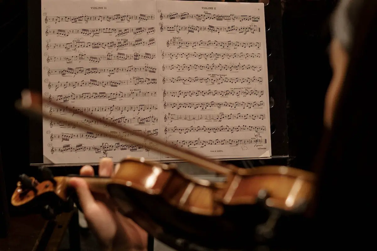 Image of a violinist in an orchestra and sheet music. Source: pexels