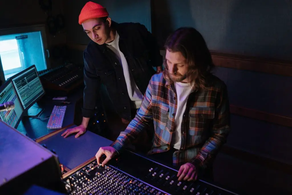 Image of two men adjusting a mixing board in a recording studio. Source: pexels