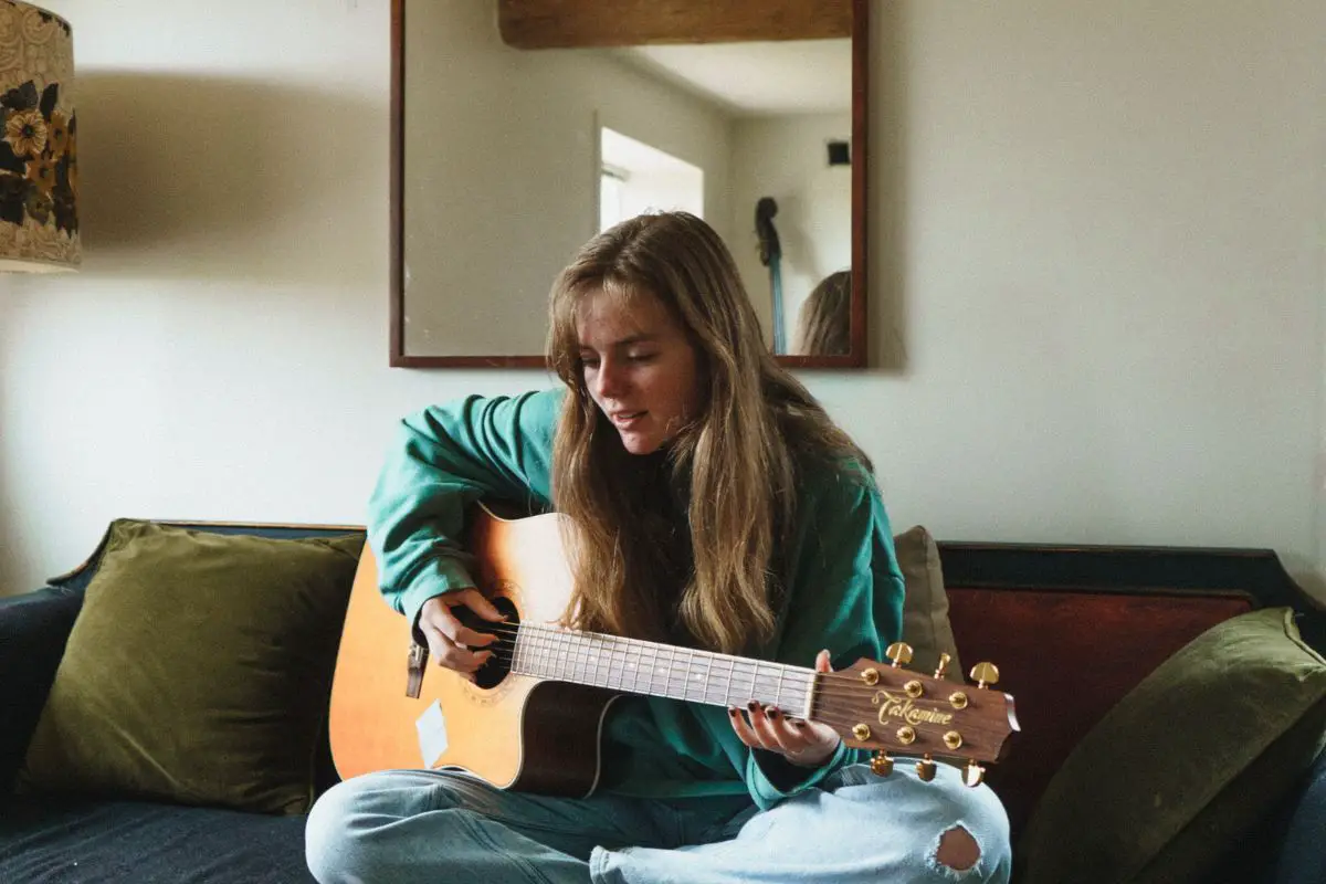 Image of a woman playing the guitar sitting in the living room.
