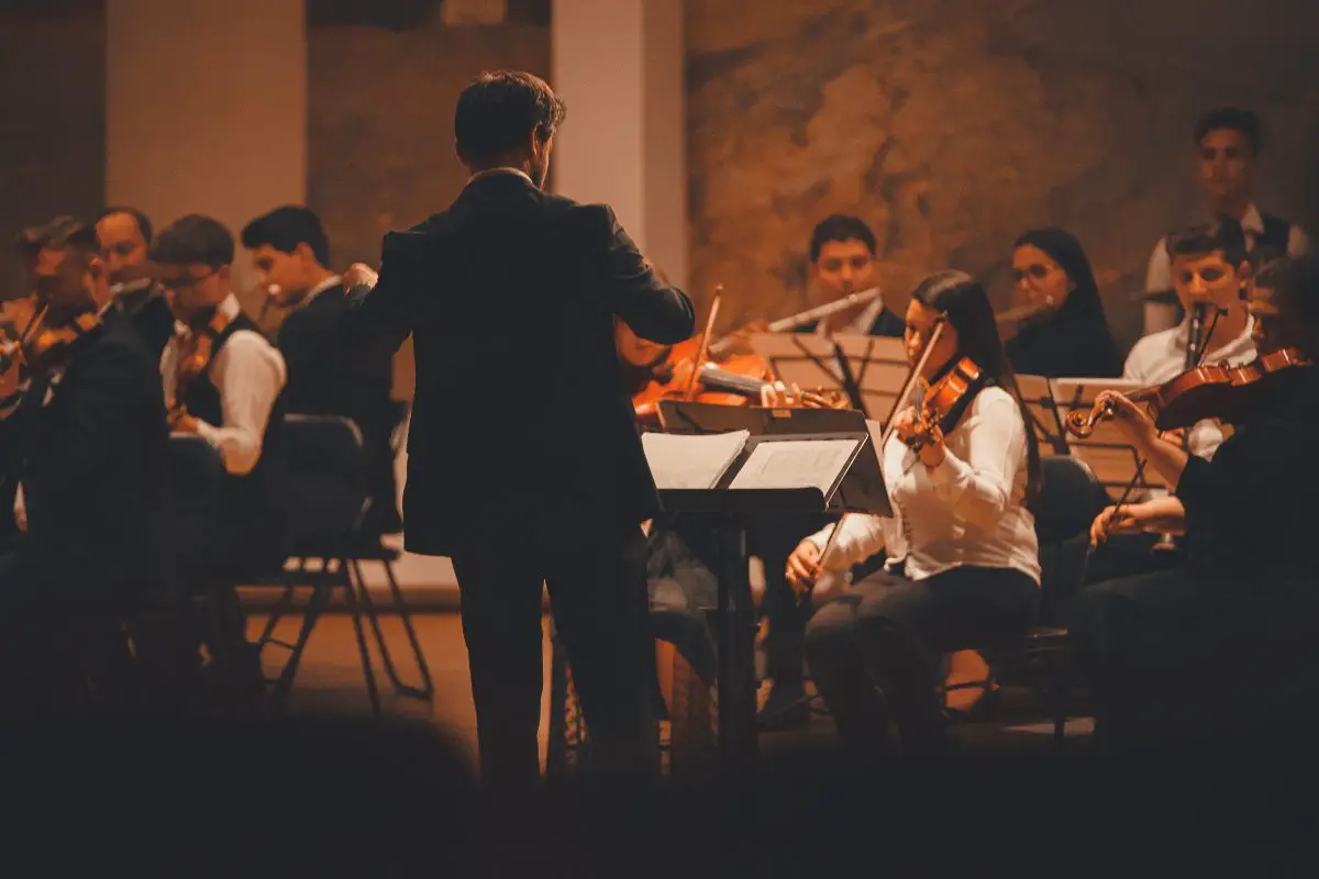 A conductor in front of an orchestra. Source: pexels
